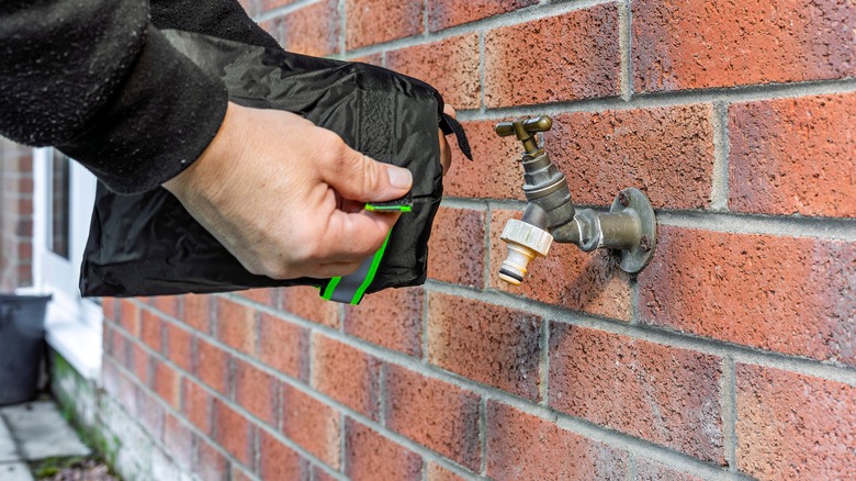 Man putting an insulating cover on a hose bib on the outside of his home