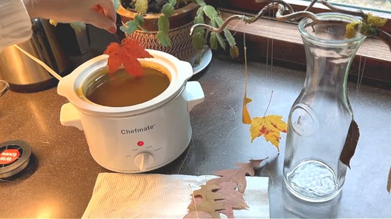 Hands dipping leaves in melted wax and drying them for decor