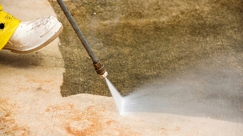 A person power washing an algae-covered concrete surface