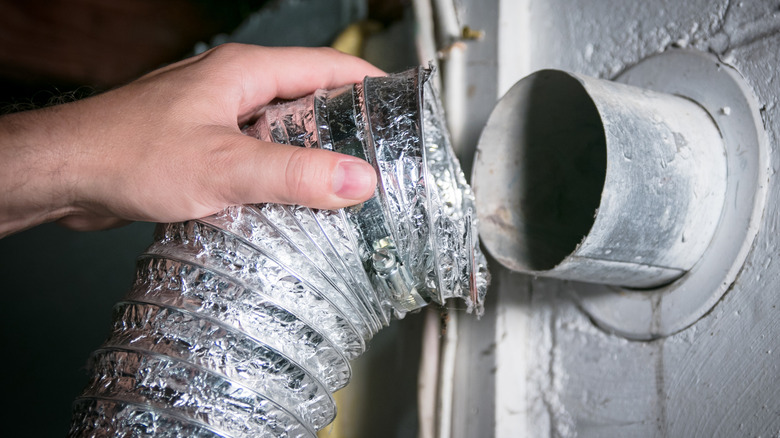 A person removing a foil dryer vent tube from the outlet pipe on the wall of a house