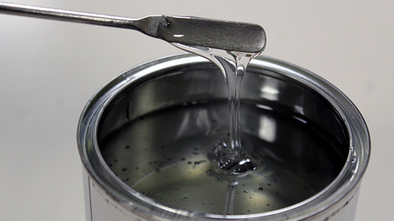 Clear resin epoxy dripping off a metal spatula into its can