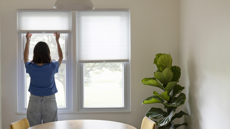 A woman opening blinds of her windows