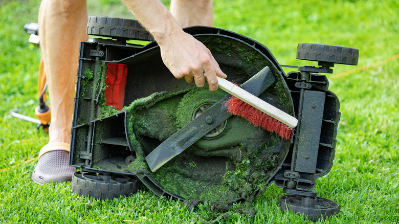 A person cleaning the underside of a mower with a brush
