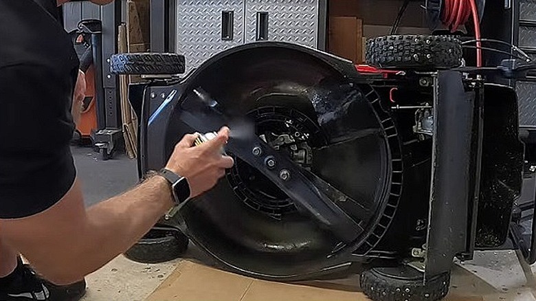 A person spraying the blades and deck of a mower with Mo-Deck