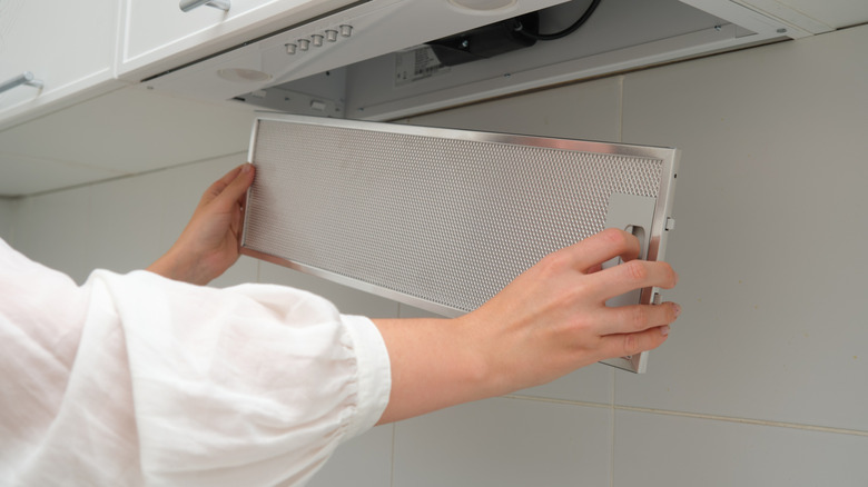 hands reinstalling a metal range hood filter