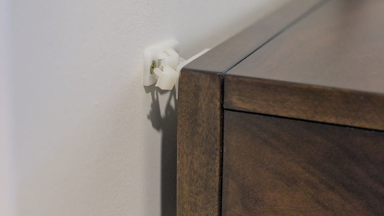 A wooden dresser secured to the wall with a white plastic and metal anti-tip kit.