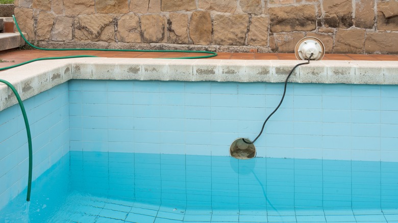 A half-filled pool being refilled by a hose