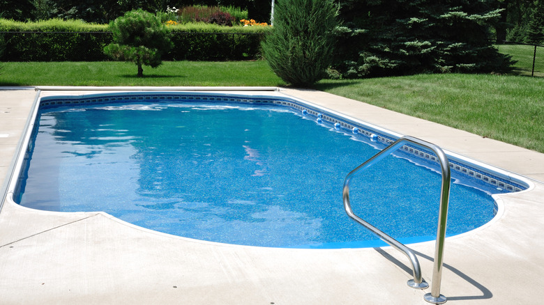 An inground pool sitting in a backyard surrounded by a lawn and shrubs