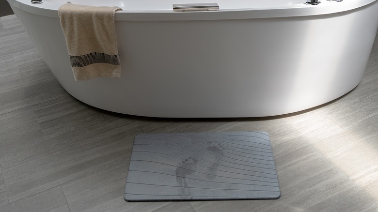 gray diatomite mat with wet footprints by white tub