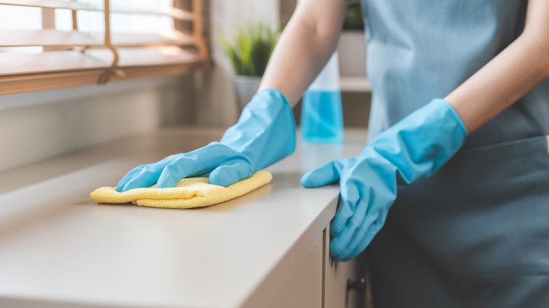 A person wearing blue rubber gloves cleaning a kitchen countertop with a yellow cloth