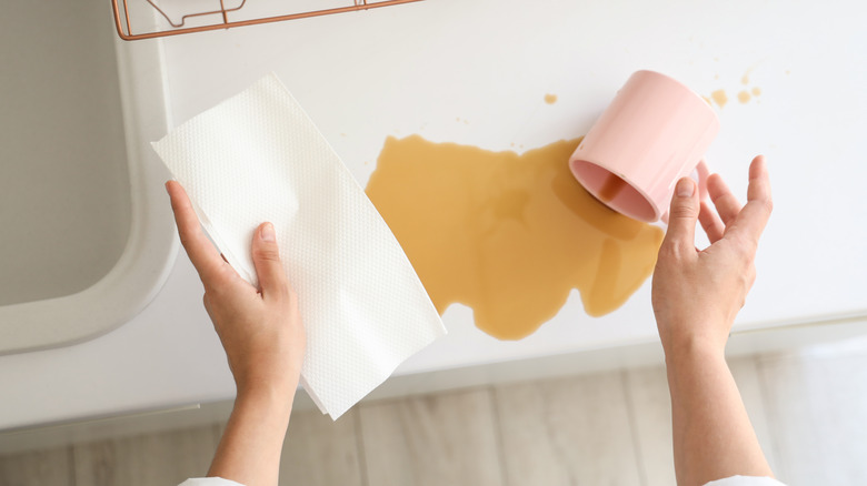 A person using a paper towel to wipe up spilled coffee on a white countertop