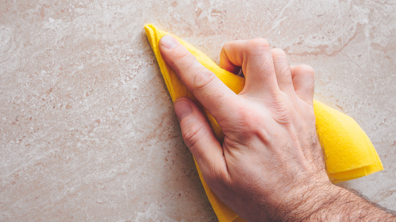 A person wiping a granite countertop with a soft yellow cloth