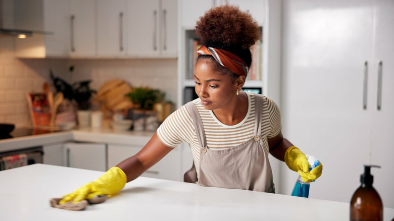 A woman holding a spray bottle wiping down a kitchen countertop
