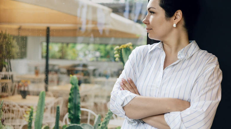 A woman worriedly looks out a window at a succulent and cactus garden that's being rained on.