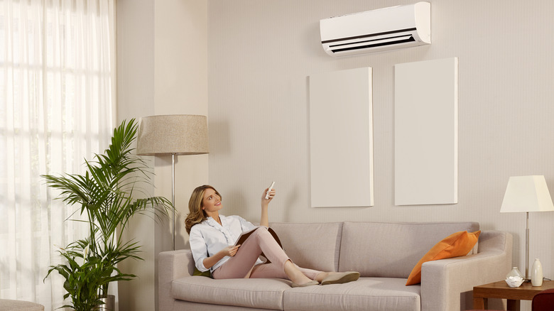 Young woman sitting and using remote control to control air conditioner in the house