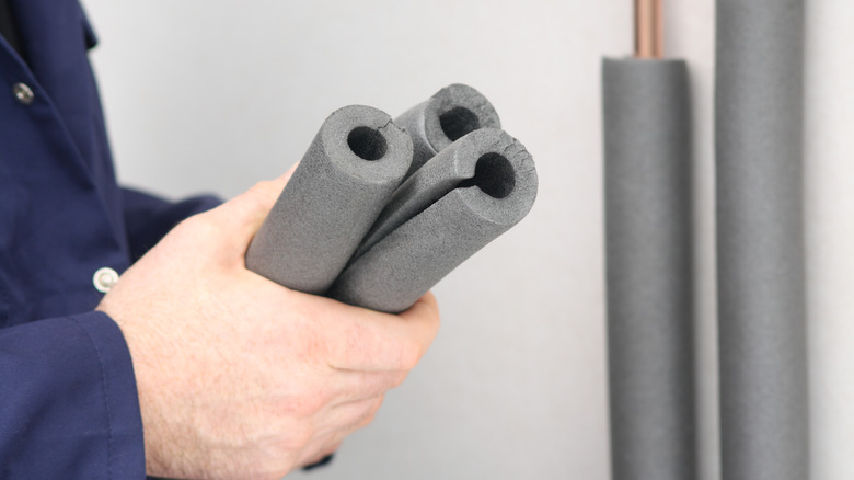 A plumber holds insulation applied to indoor copper water pipes.