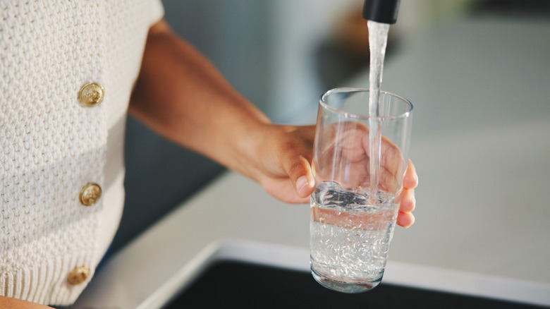 Woman pouring glass of water from faucet