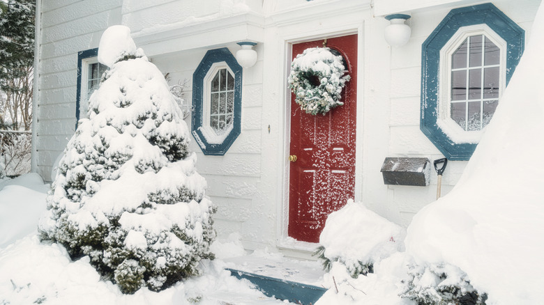 House exterior with red wooden door covered in snow