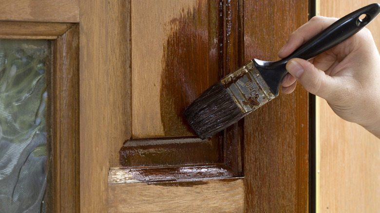 Close-up of a person treating applying sealant to a wooden door with a brush