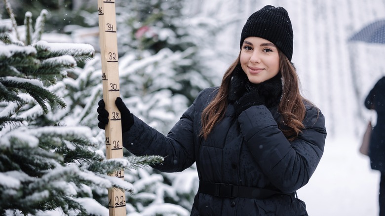 A woman uses a measuring stick to pick out a Christmas tree