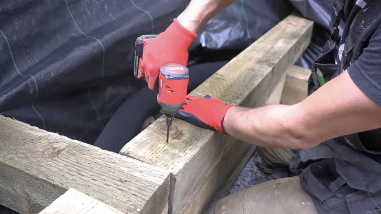 Person uses their drill to secure a wood post while building a wood retaining wall.