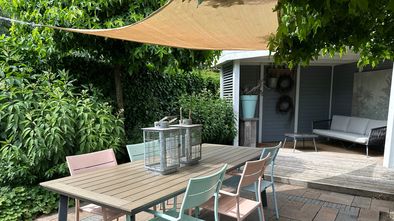 A residential patio with a tan shade sail above the outdoor dining table.
