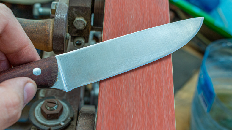 a person sharpening the blade of knife on a belt sander