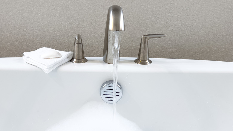 A nickel faucet filling up a soapy bathtub with water