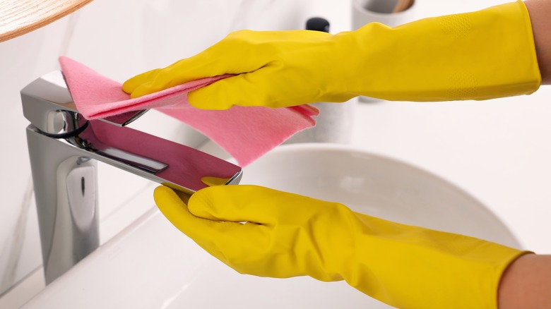 Hands in gloves wiping down a bathroom faucet.