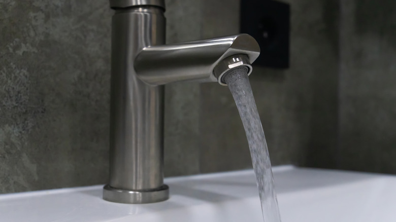 A brushed nickel faucet flowing water into a sink.