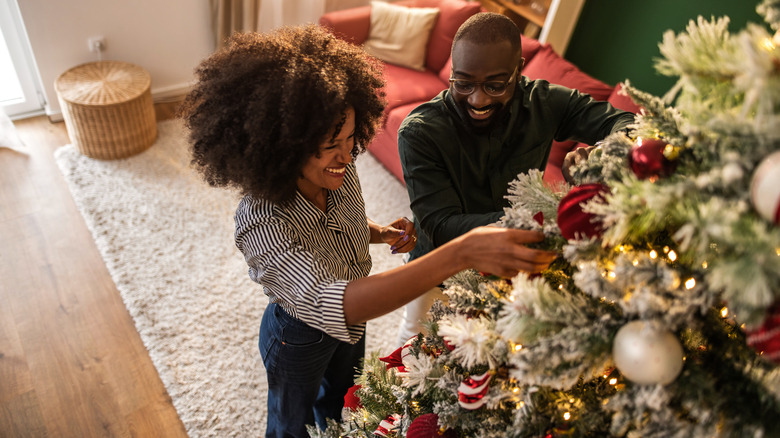 A smiling couple hangs vintage ornaments on a Christmas tree