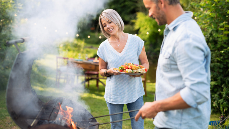 Two people standing around a very smoky grill