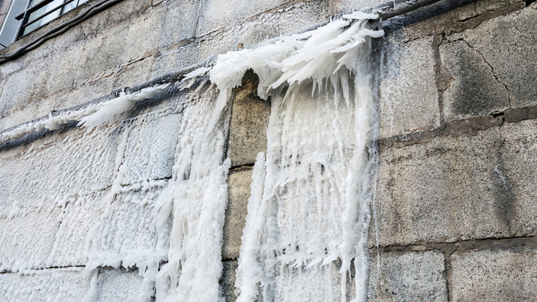 A burst pipe along the side of a brick building, with ice crawling down the wall and sticking out of the pipe