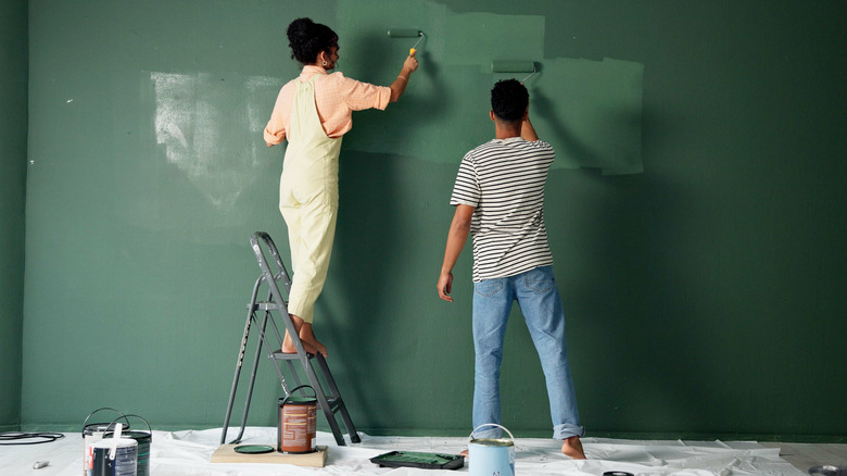 A couple paints a feature wall with a deep green paint.