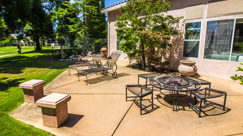 A stained concrete patio filled with different styles of outdoor furniture in a large backyard.