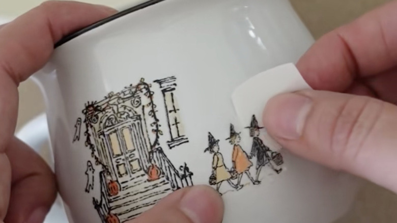 woman putting witch decal onto ceramic mug