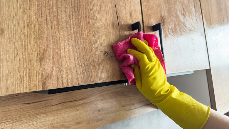 A man cleaning kitchen cabinets above the stove