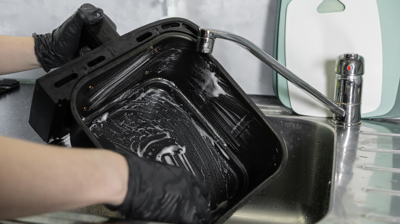 Black-gloved hands cleaning an air fryer basket
