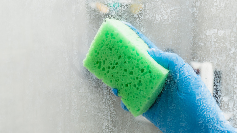 Close up of person wiping shower door with green sponge