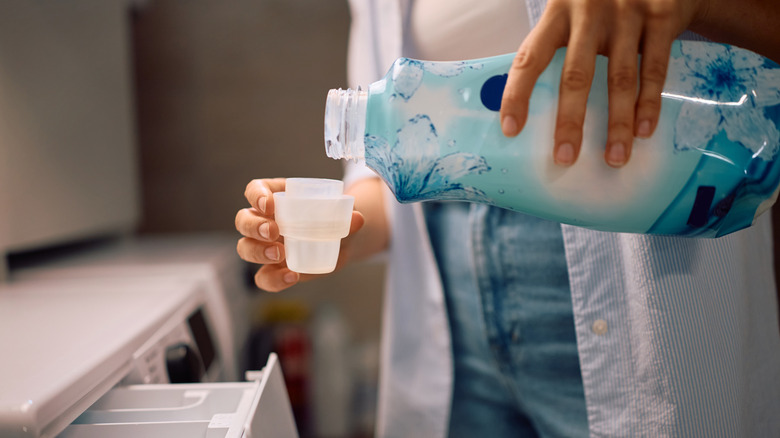 Close-up of woman pouring fabric softener to use in the washing machine in a laundry room, highlighting a common step in one's laundry routine.
