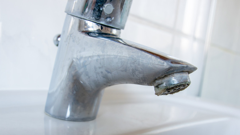 Close-up of a bathroom faucet coated with chalky white limescale film