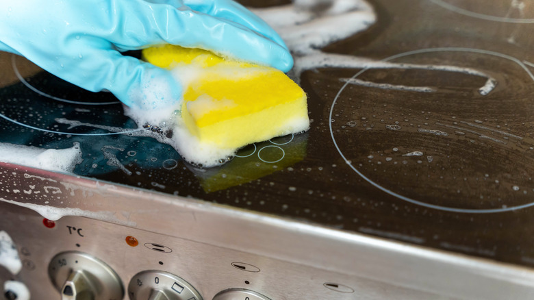 Hand using sponge to clean a glass stovetop