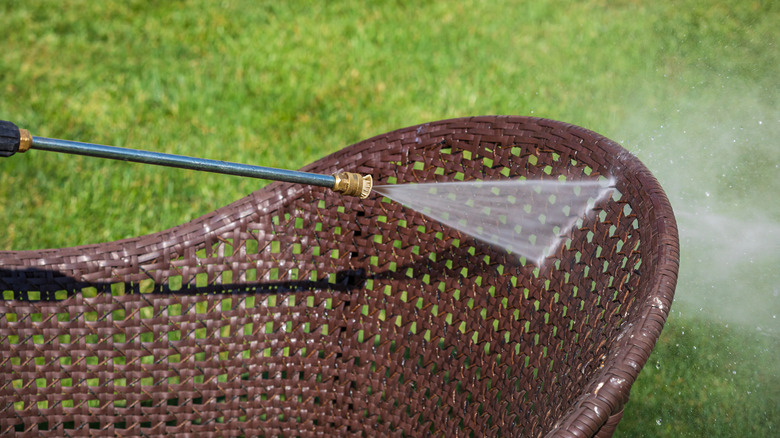 person pressure washing outdoor wicker chair
