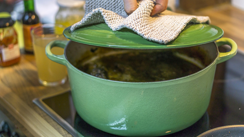 A hand taking the lid off a green enameled cast-iron pot