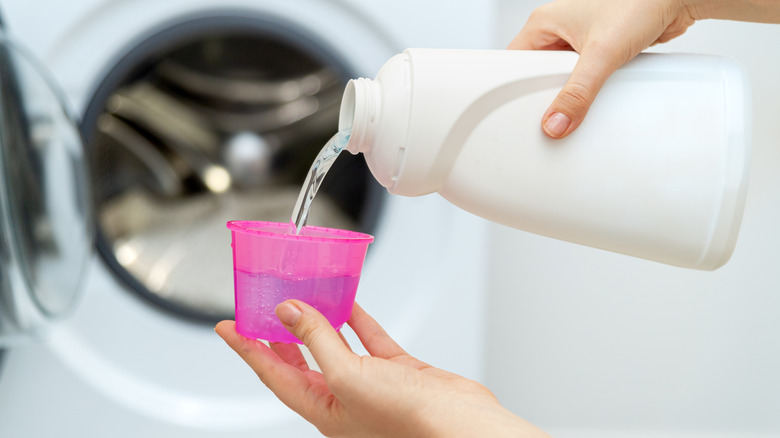 Close up of person pouring laundry detergent into cap in front of washing machine