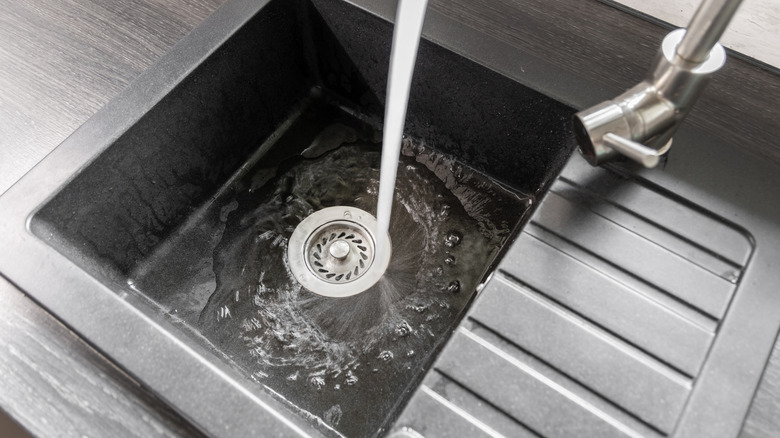 Water from a faucet runs down a dark composite sink that has just been cleaned.