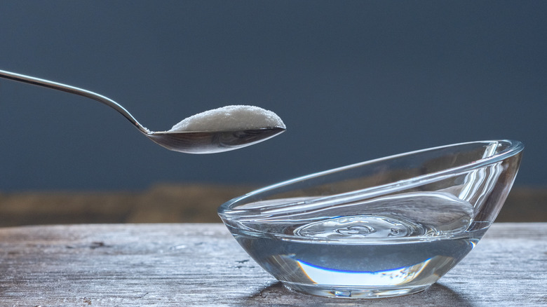 Close-up of a spoon with salt held over a bowl filled with white vinegar