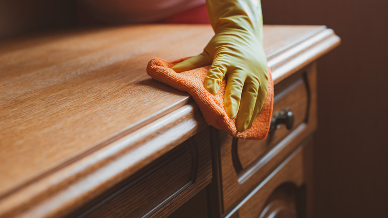 Close-up of a person cleaning a wood desk with a rag