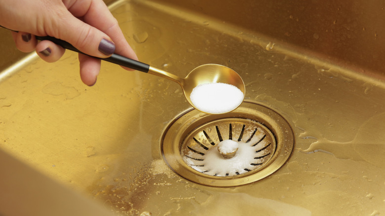 Hand with painted nails pouring salt into a sink drain
