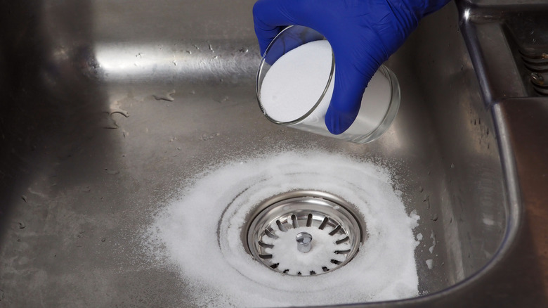 Gloved hand pouring a cup of baking soda down a drain